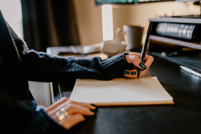 A hand holding a pen over an open notebook with soft morning light