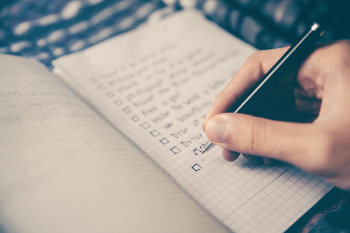 A person writing a list by hand in an open notebook on a desk