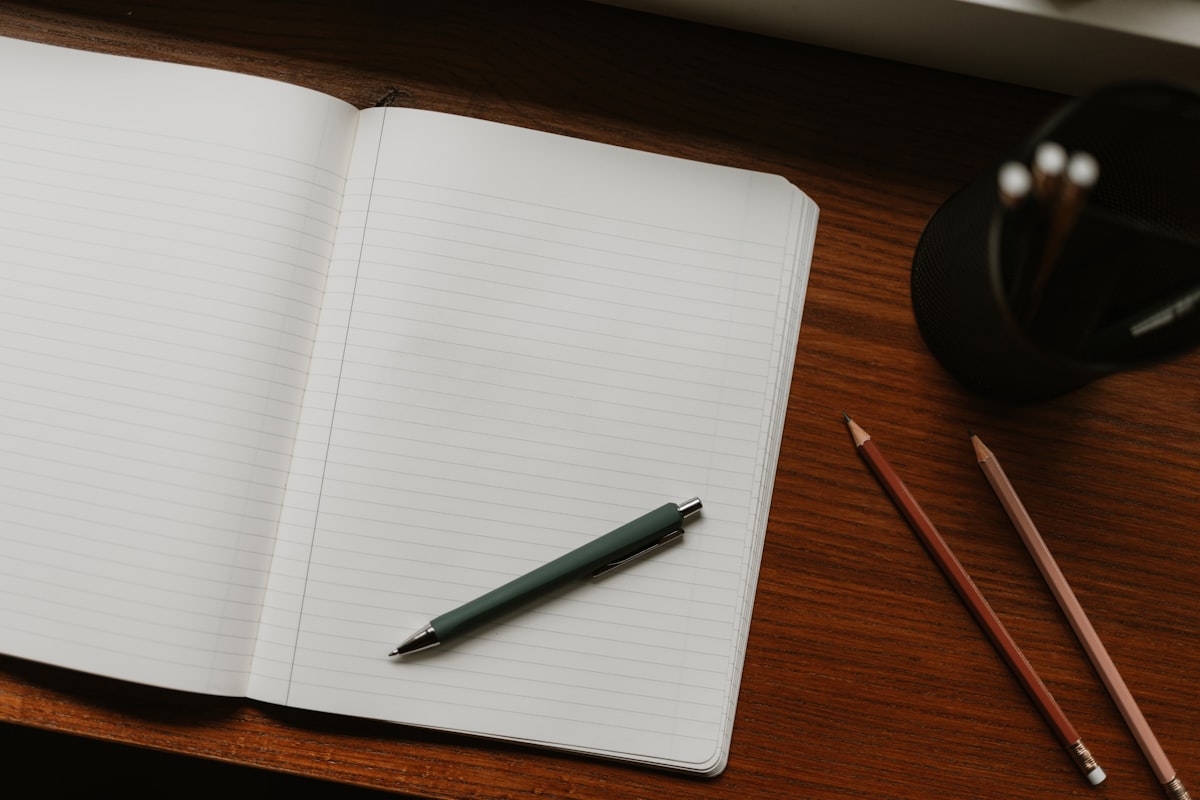 An open handwritten notebook beside a laptop keyboard on a wooden desk in soft natural light