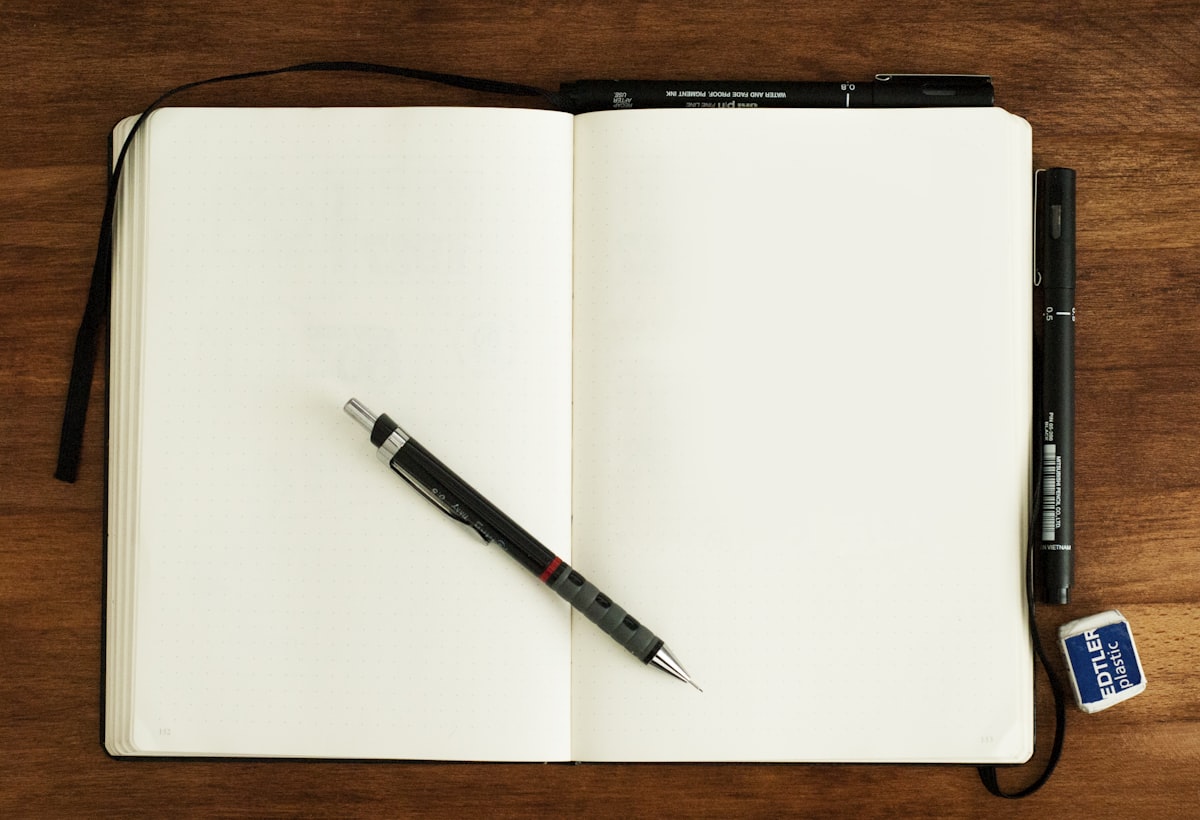 A black and silver pen resting on a blank open notebook in calm morning light