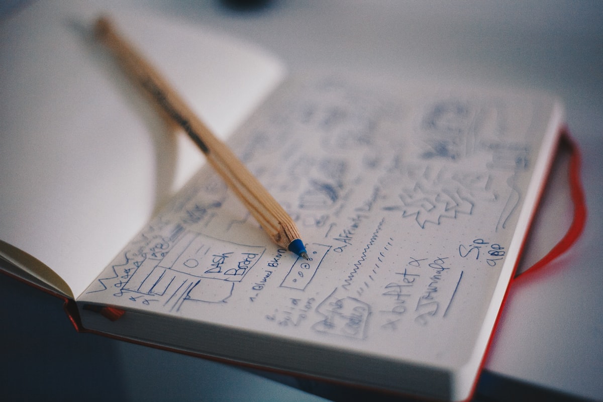 An open notebook with a single colored pencil, half-filled page with sketches and scattered words