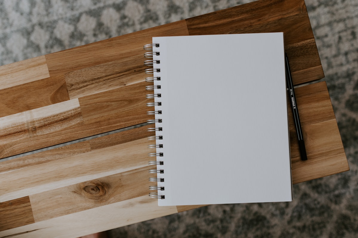 A white spiral notebook resting on a brown wooden table, one of many kept over the years